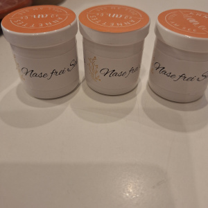 drei weiße Salbendosen mit Aufdruck Nase frei auf heller Fläche